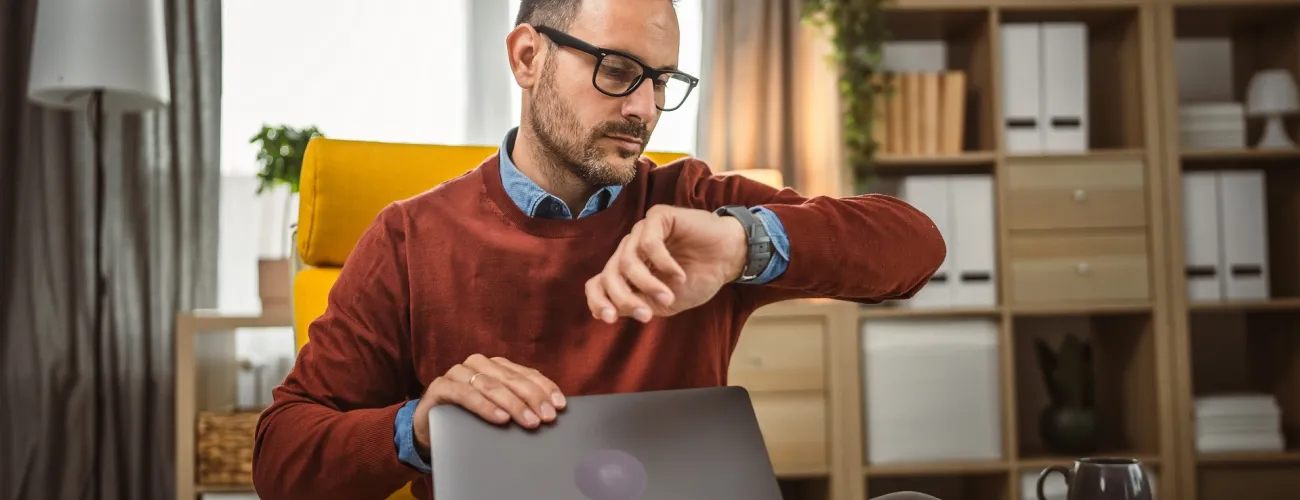 Un homme regarde l'heure en fermant son ordinateur
