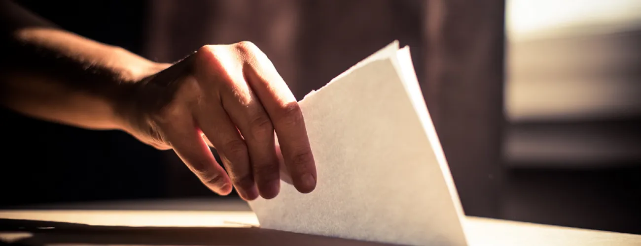 main déposant un bulletin de vote dans une urne