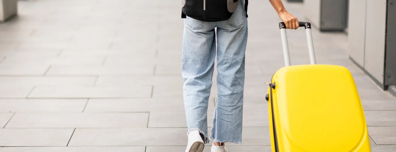 femme de dos tirant une valise jaune