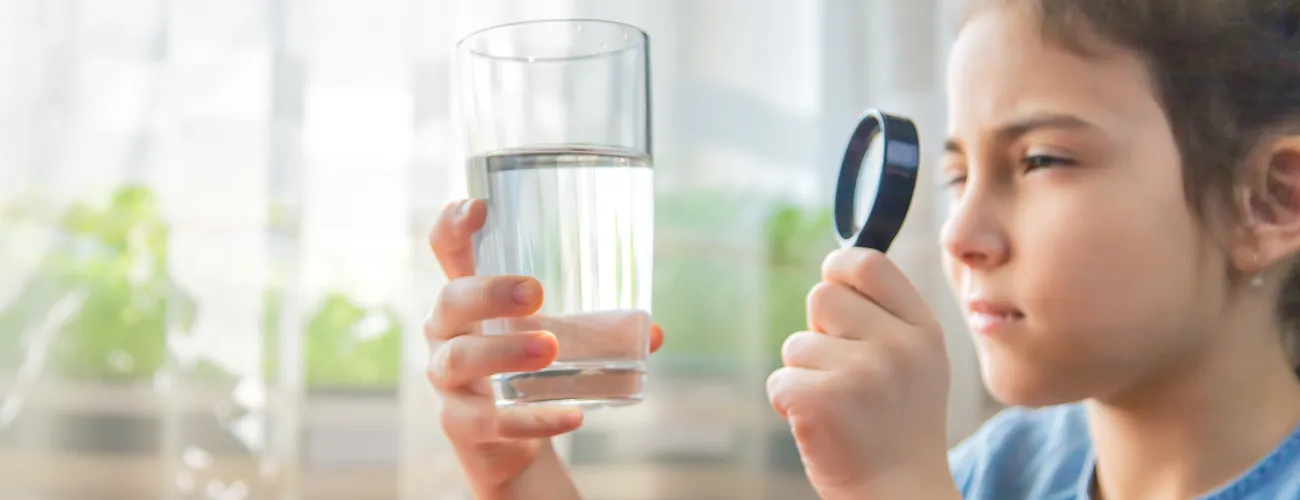 une petite fille inspecte un verre d'eau avec une loupe