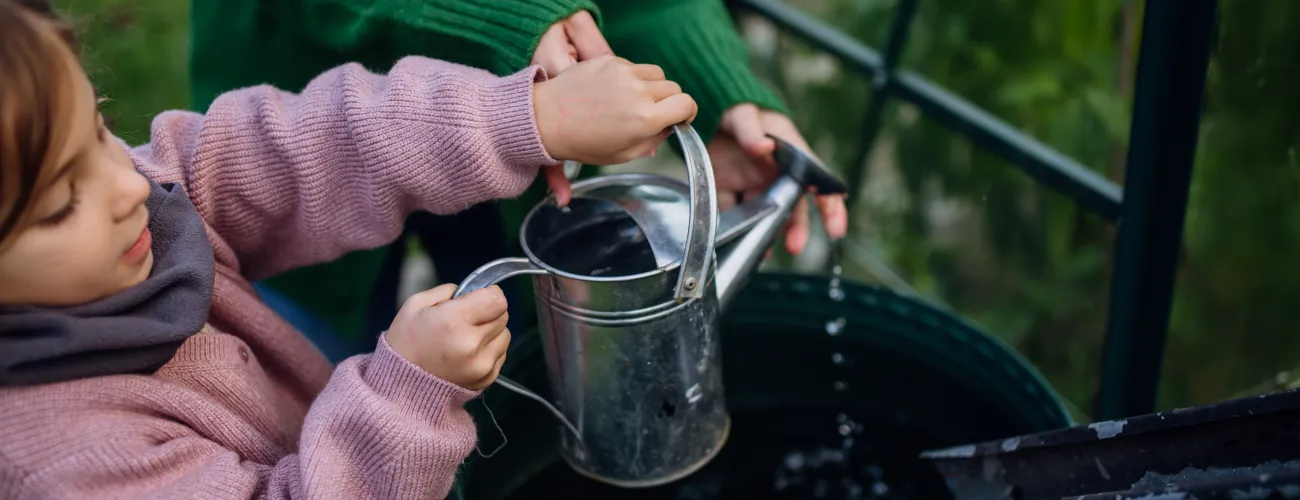 Une fillette et sa maman récupèrent de l'eau de pluie dans un arrosoir. 