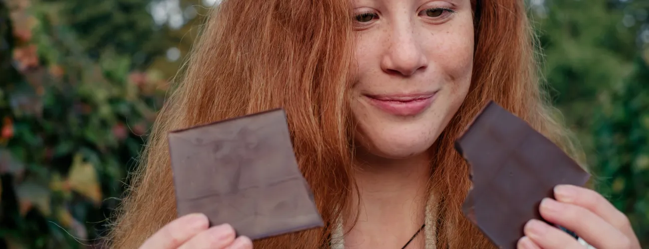 une jeune femme rousse regarde deux morceaux de chocolat