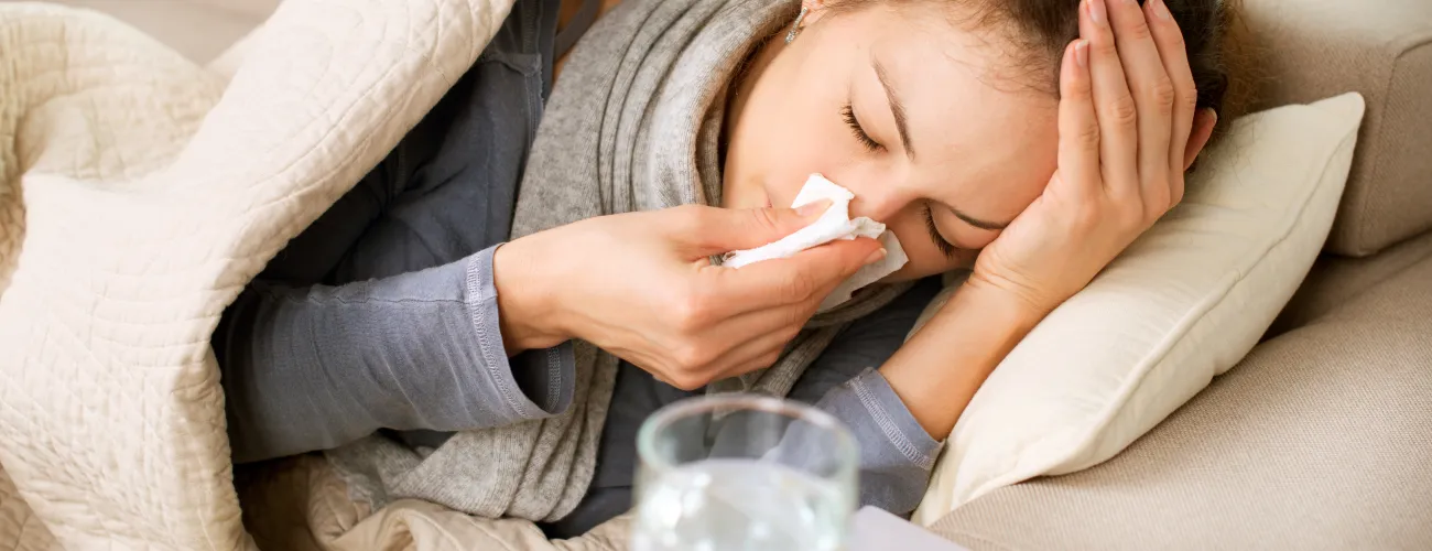 une femme malade se mouche le nez couchée sous une couverture