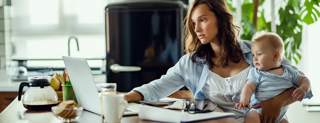 Une femme regarde un document, l'air fatigué et un bébé dans les bras.