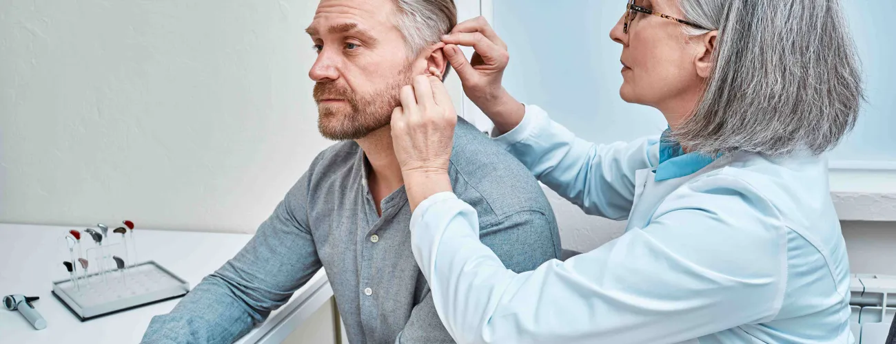 Une audicienne place un appareil auditif dans l'oreille d'un monsieur