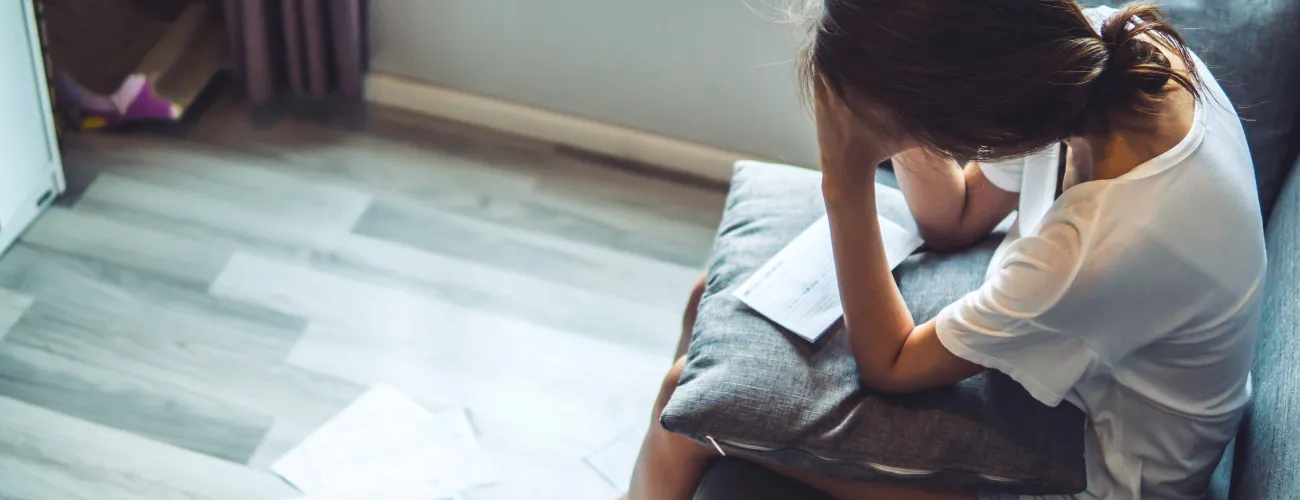 Une jeune femme se prend la tête dans les mains devant un amas de factures qui s'accumulent