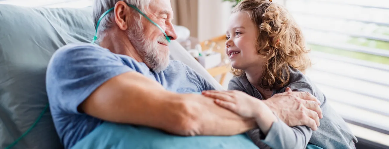 un monsieur alité sur un lit d’hôpital parle avec sa petite fille