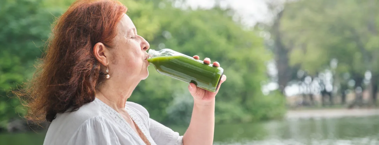 une vieille femme boit un jus de légumes