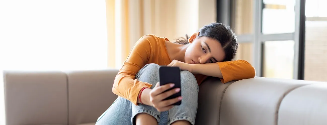 Une jeune fille dans un canapé regarde avec ennui son téléphone.