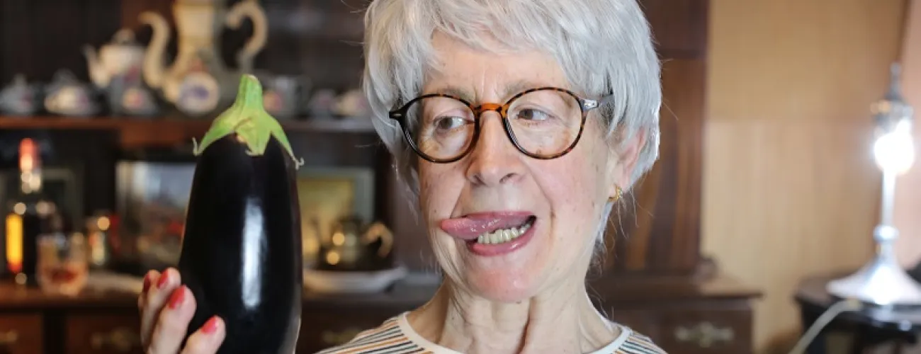 Une senior tient une aubergine en main en la regardant d'un air coquin.
