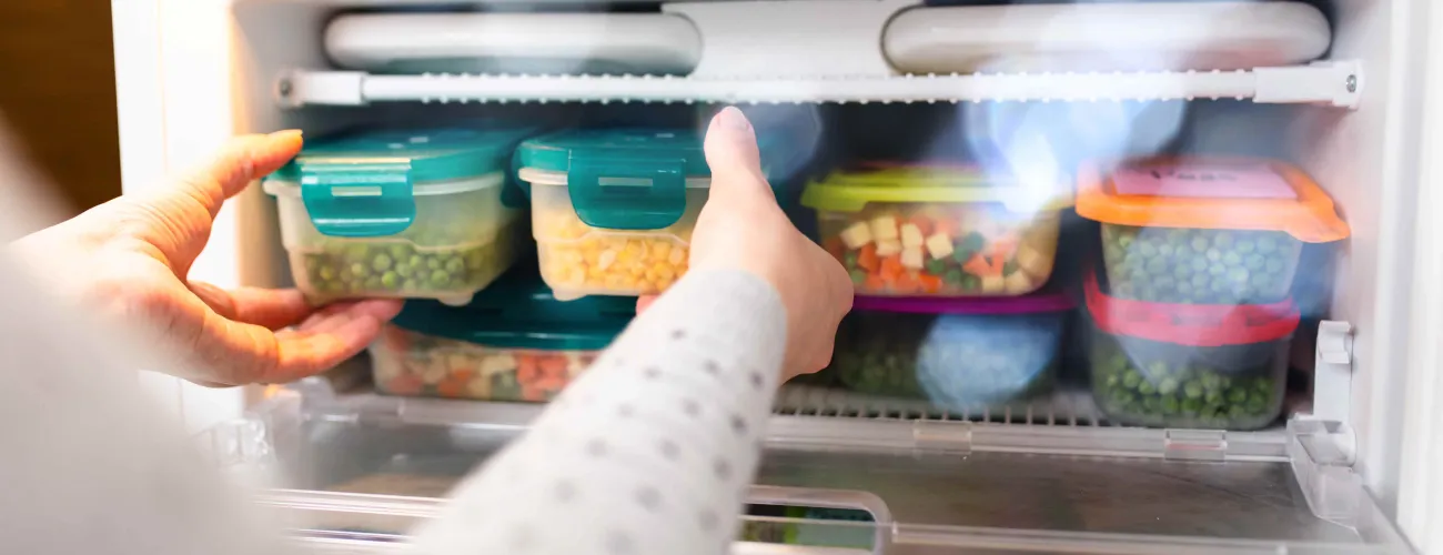 une dame prend des boites d'aliments au congélateur