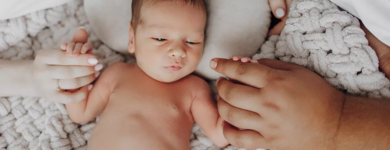 un bébé entouré des mains de ses parents