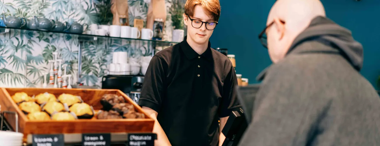 Un étudiant vend du pain à un client dans une boulangerie