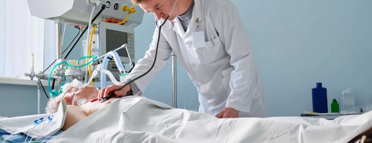 Un médecin vérifie le coeur d'un patient couché dans un lit et relité à une machine respiratoire