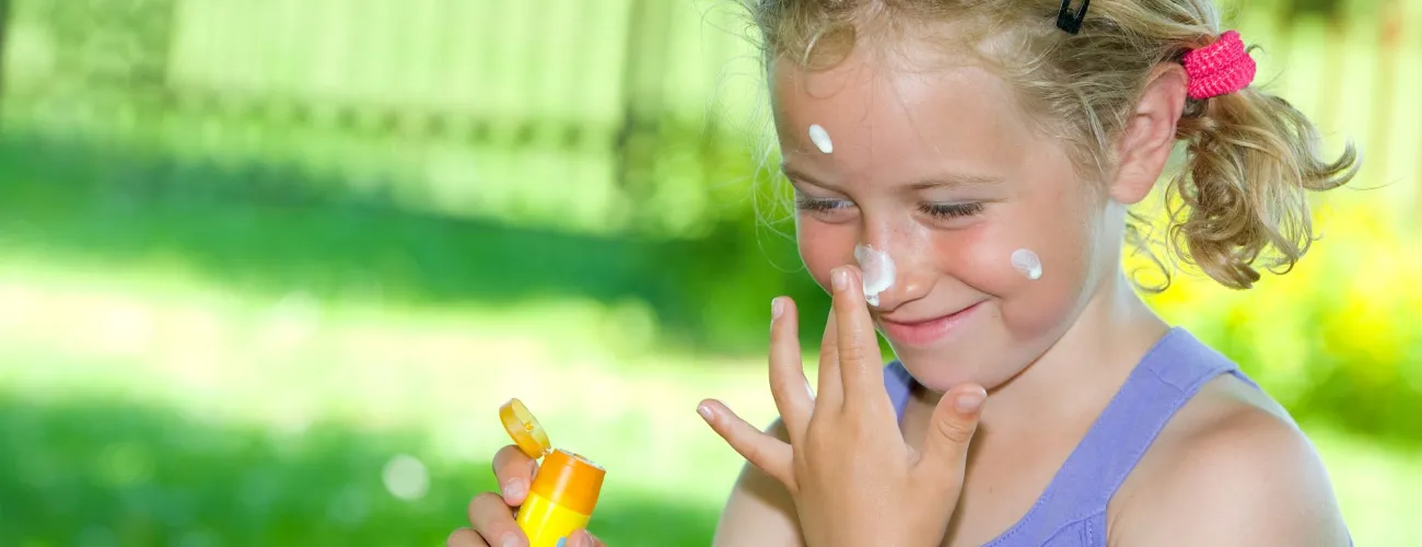 une petite fille s'applique de la crème solaire sur le visage