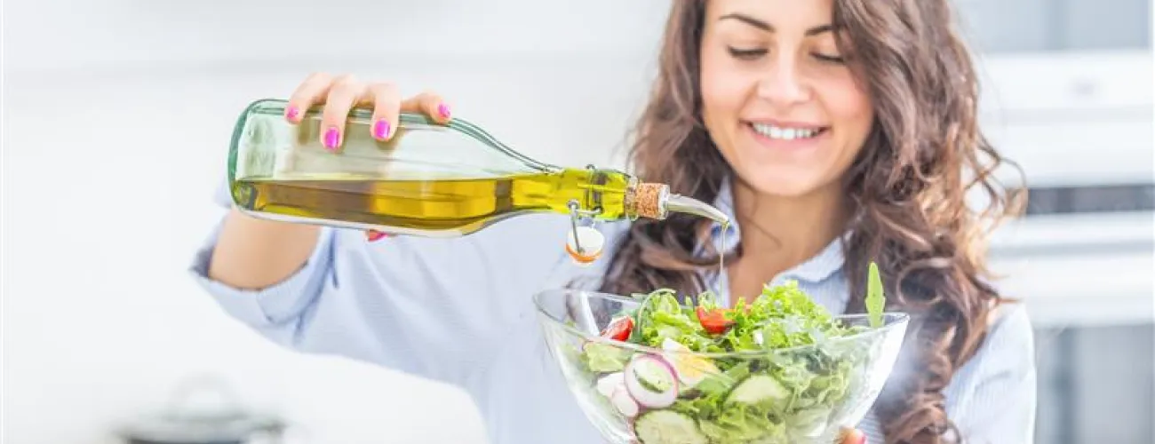 une jeune femme fait couler de l'huile d'olive dans la salade