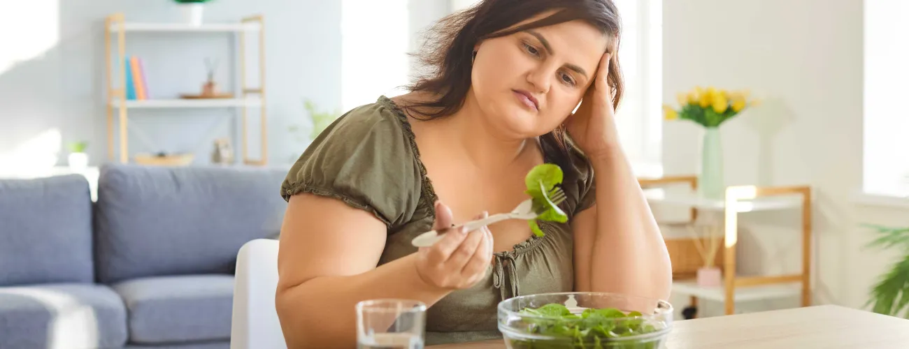 Une jeune femme mange avec désintérêt une salade 