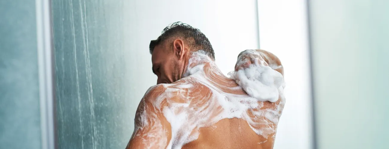 Un homme, de dos, se lave sous la douche