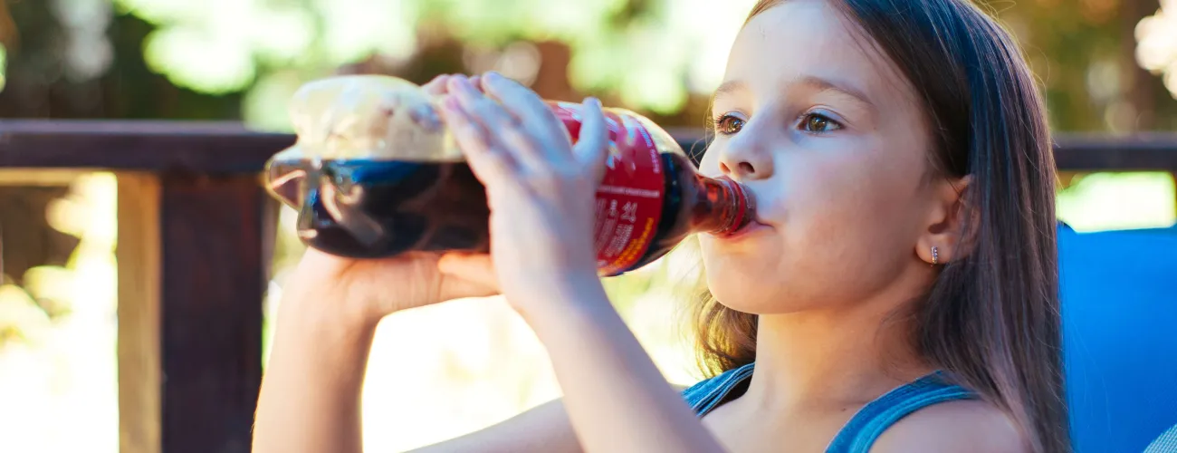 une enfant boit à la bouteille de coca