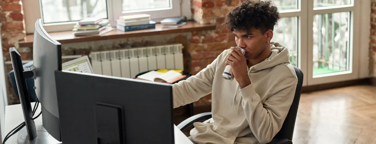 Un jeune homme boit une canette d'Energy Drink devant son ordinateur