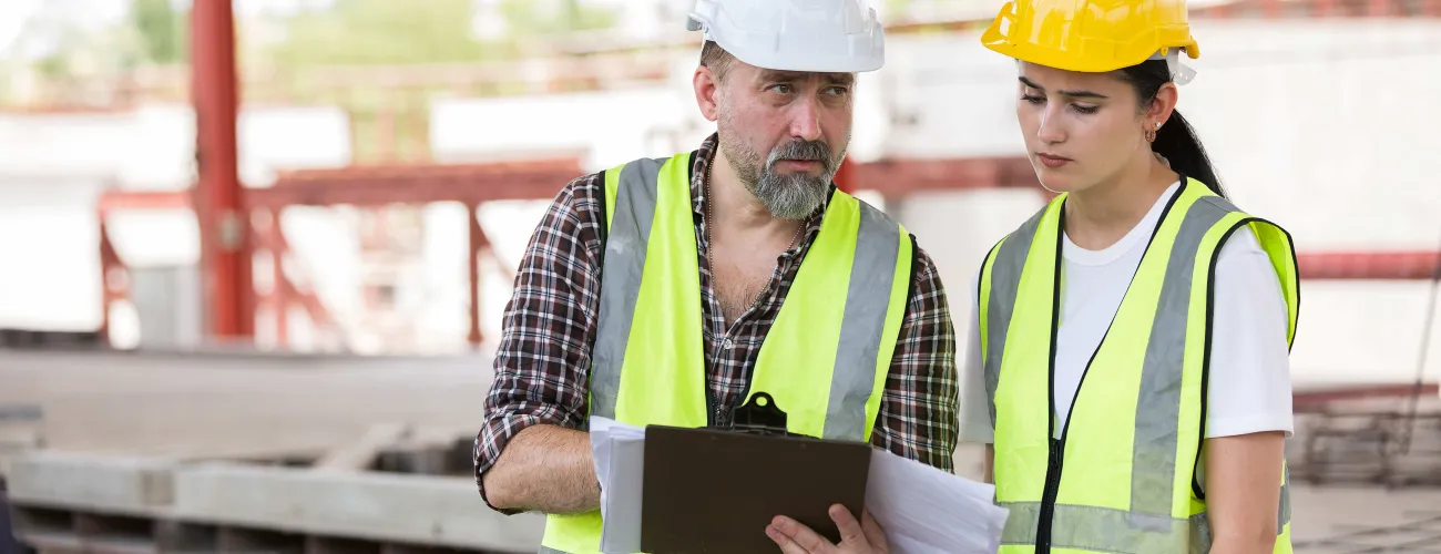 Une femme et son collègue regardent ensemble un document sur chantier