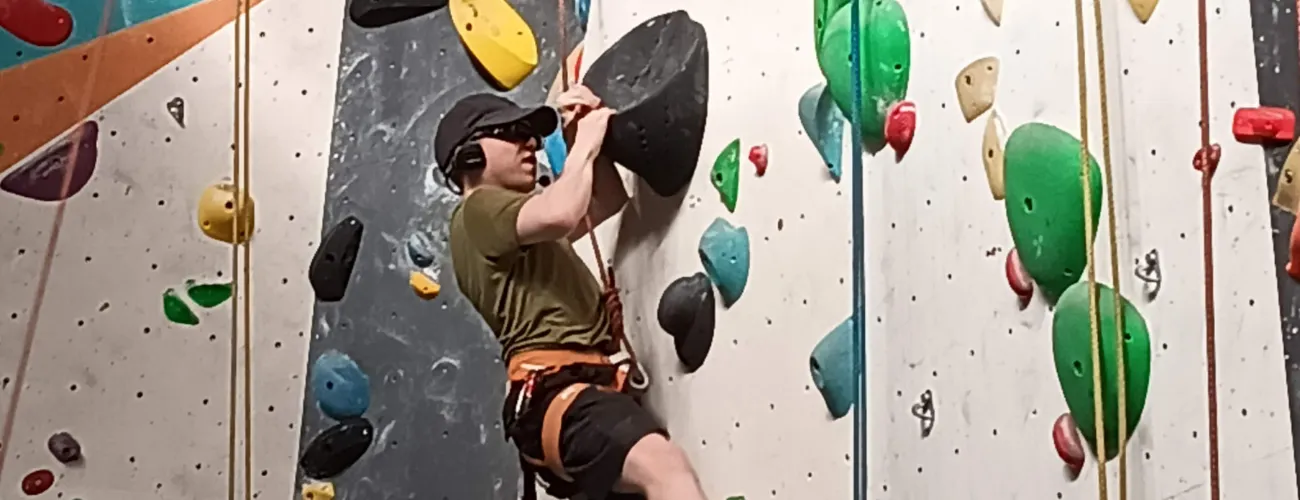 Tristan, malvoyant et malentendant, progresse sur la paroi grâce à un dispositif audio adapté qui le relie à son coach resté en bas.