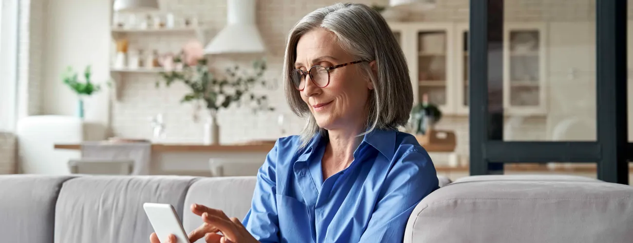 Une dame assise dans son fauteuil regarde son écran de téléphone