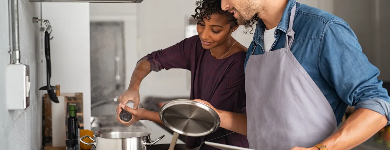 Un couple cuisine et ajoute du sel dans une casserole