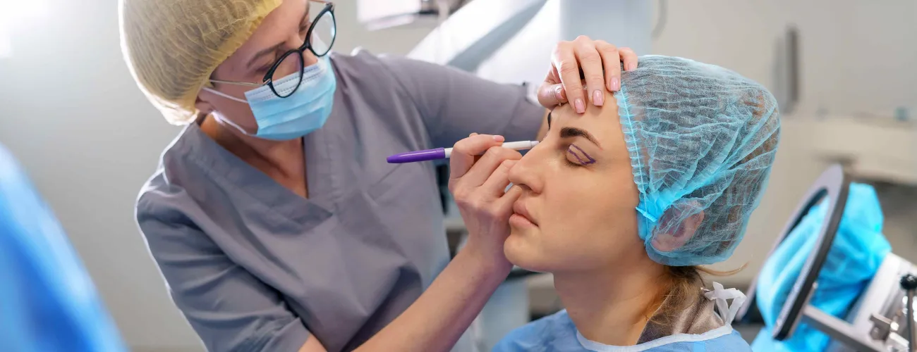 un chirurgien dessine des traits sur le visage d'une patiente avant l'opération.