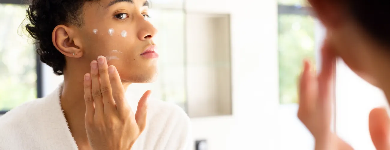 Un adolescent met de la crème sur sa peau