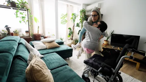 Une mère porte son fils dans les bras pour le déplacer du fauteuil roulant au canapé