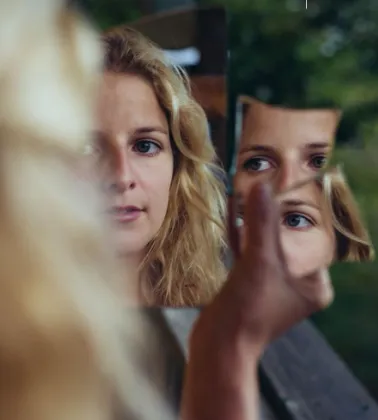 Une jeune femme se regarde dans un miroir brisé