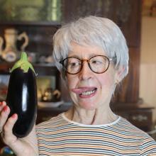 Une senior tient une aubergine en main en la regardant d'un air coquin.