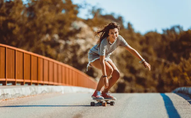 Jeune femme fait du skateboard sur une route ensoleillée